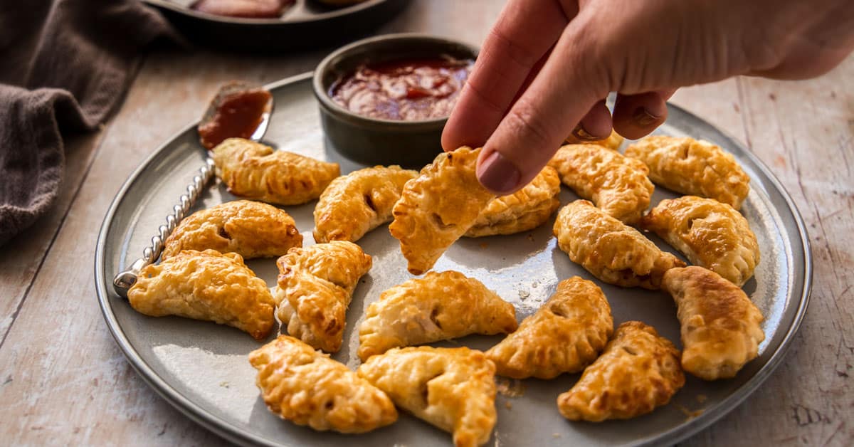 plate of mini bacon pasties with a hand picking up a pasty.