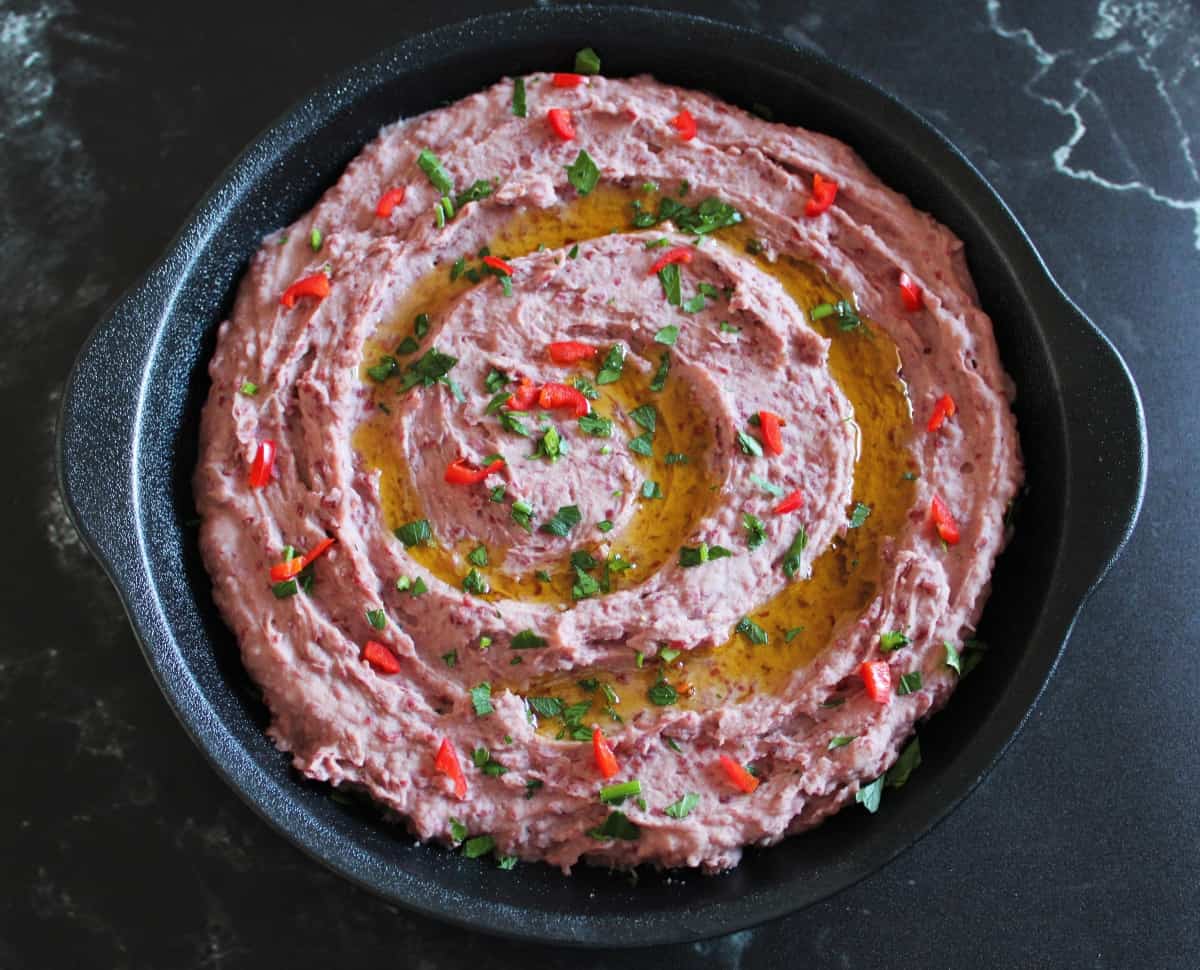 Red kidney bean dip in a black dish sitting on a black marble background.