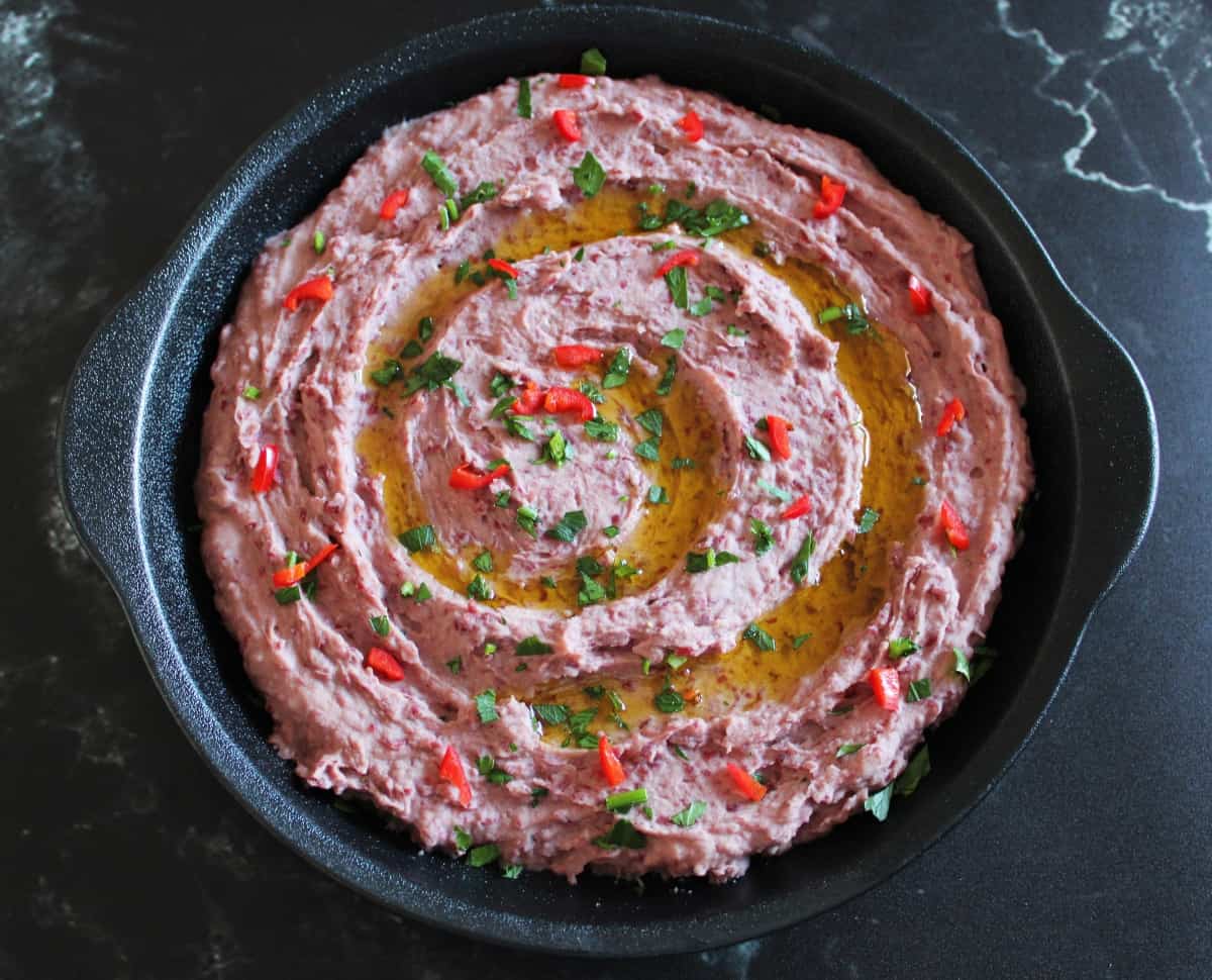  Red kidney bean dip i en sort skål sidder på en sort marmor baggrund.