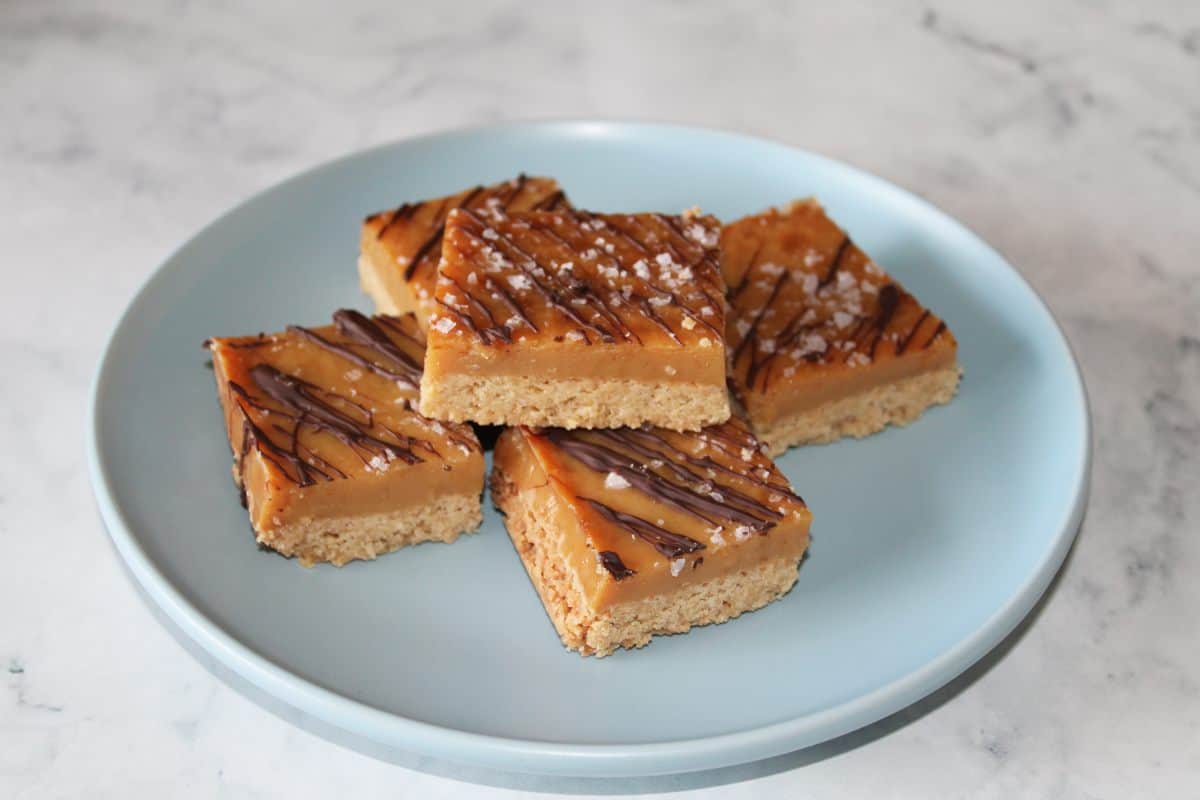 Five pieces of caramel slice on a round blue plate sitting on a marble bench.