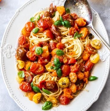 large white platter of pasta, topped with roasted tomato sauce and garnished with basil leaves. silver spoon on edge of dish.