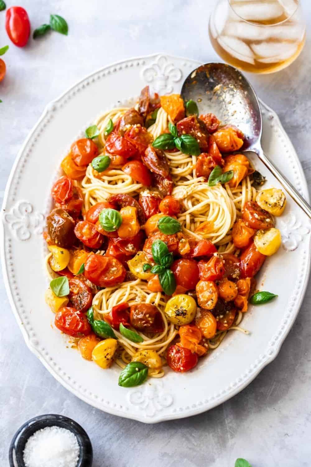 large white platter of pasta, topped with roasted tomato sauce and garnished with basil leaves. silver spoon on edge of dish.