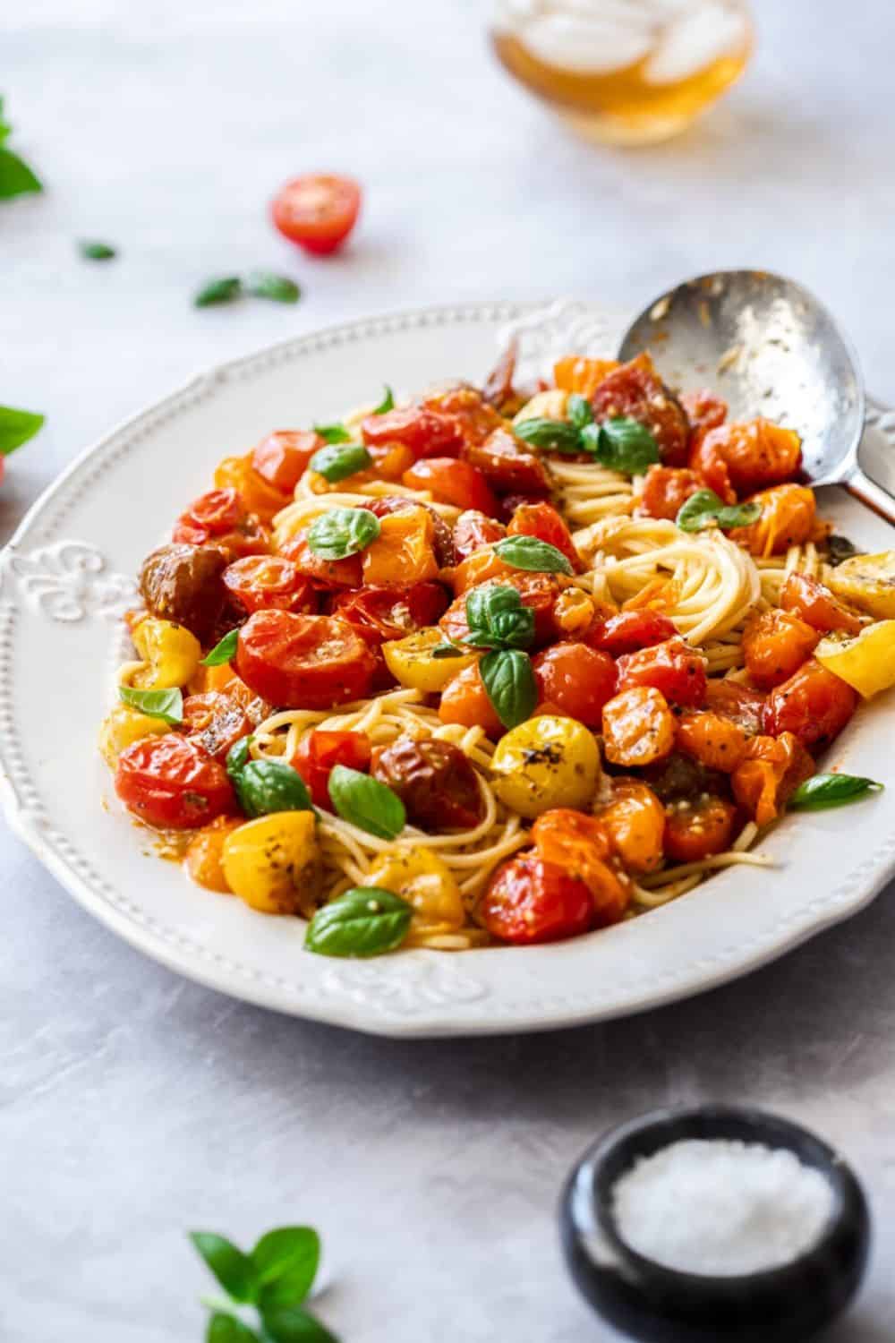 large white platter of pasta, topped with roasted tomato sauce and garnished with basil leaves. silver spoon on edge of dish.