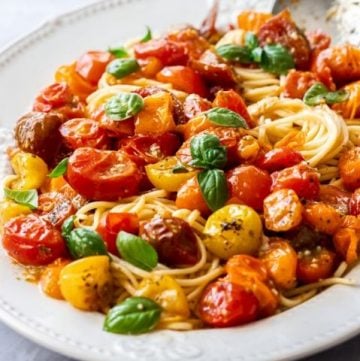 large white platter with pasta, topped with roasted tomatoes and fresh basil leaves.