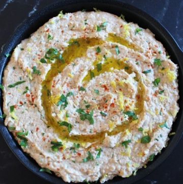 Black dish of tuna and white bean dip on black marble background.