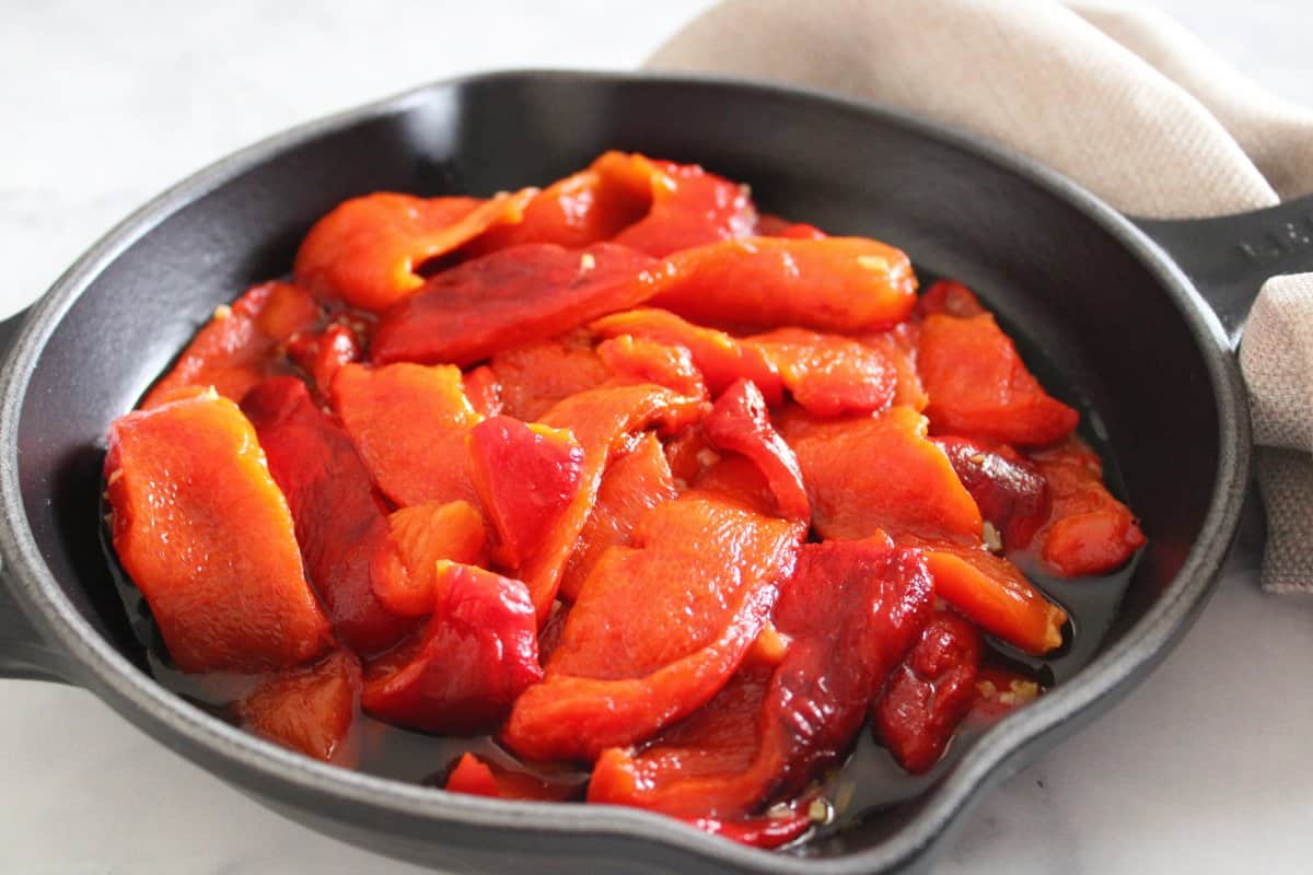 Black skillet with roasted peppers, with a beige napkin on a marble background.