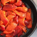 Black skillet with roasted peppers, with a beige napkin.