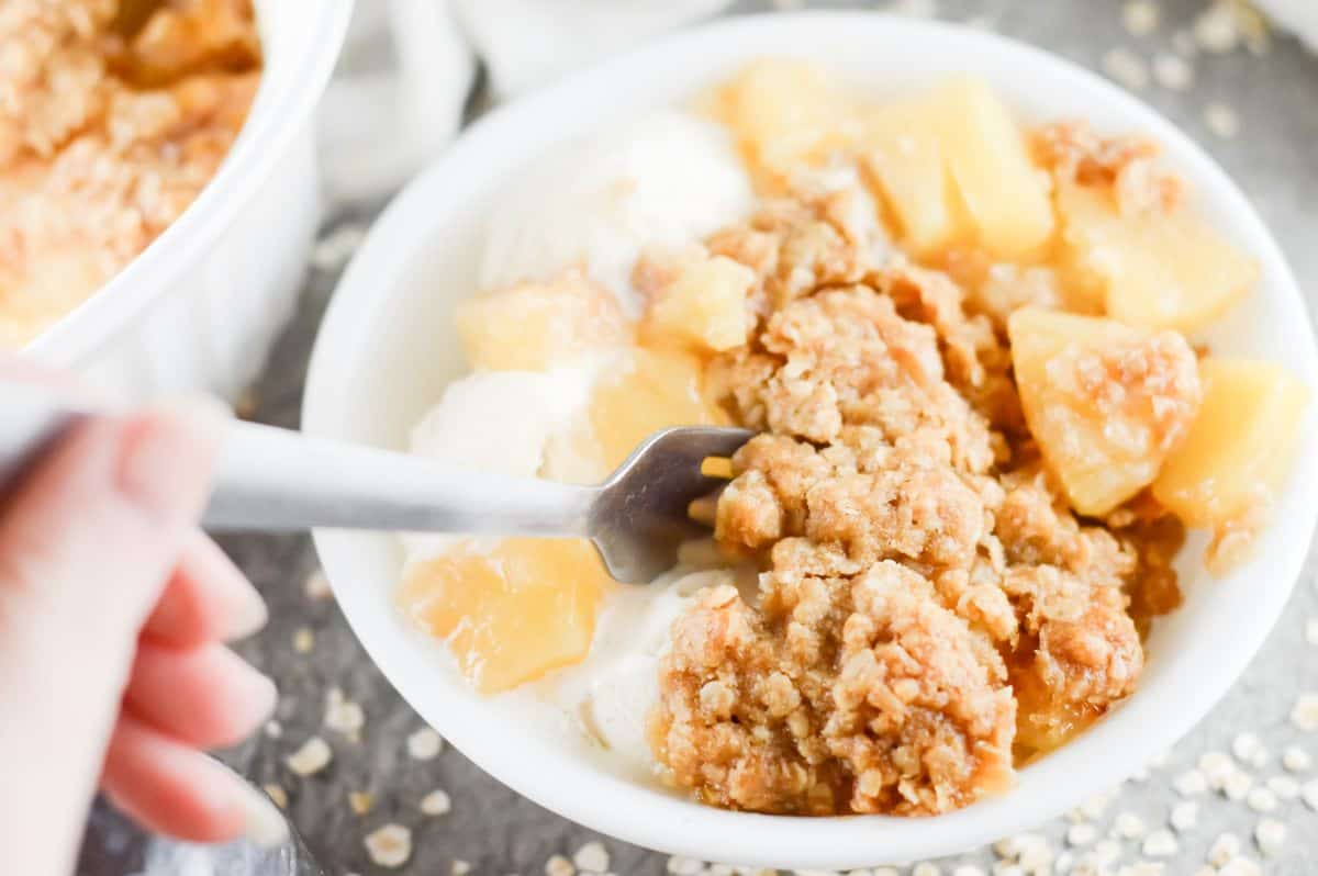 bowl of pineapple crisp, with a hand holding a fork.