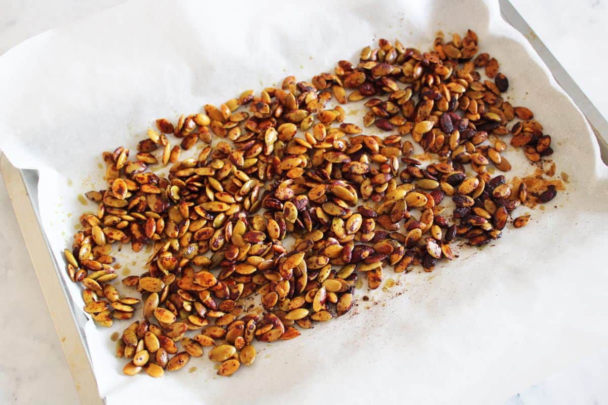 roasted pepitas on baking paper sitting on a baking sheet.