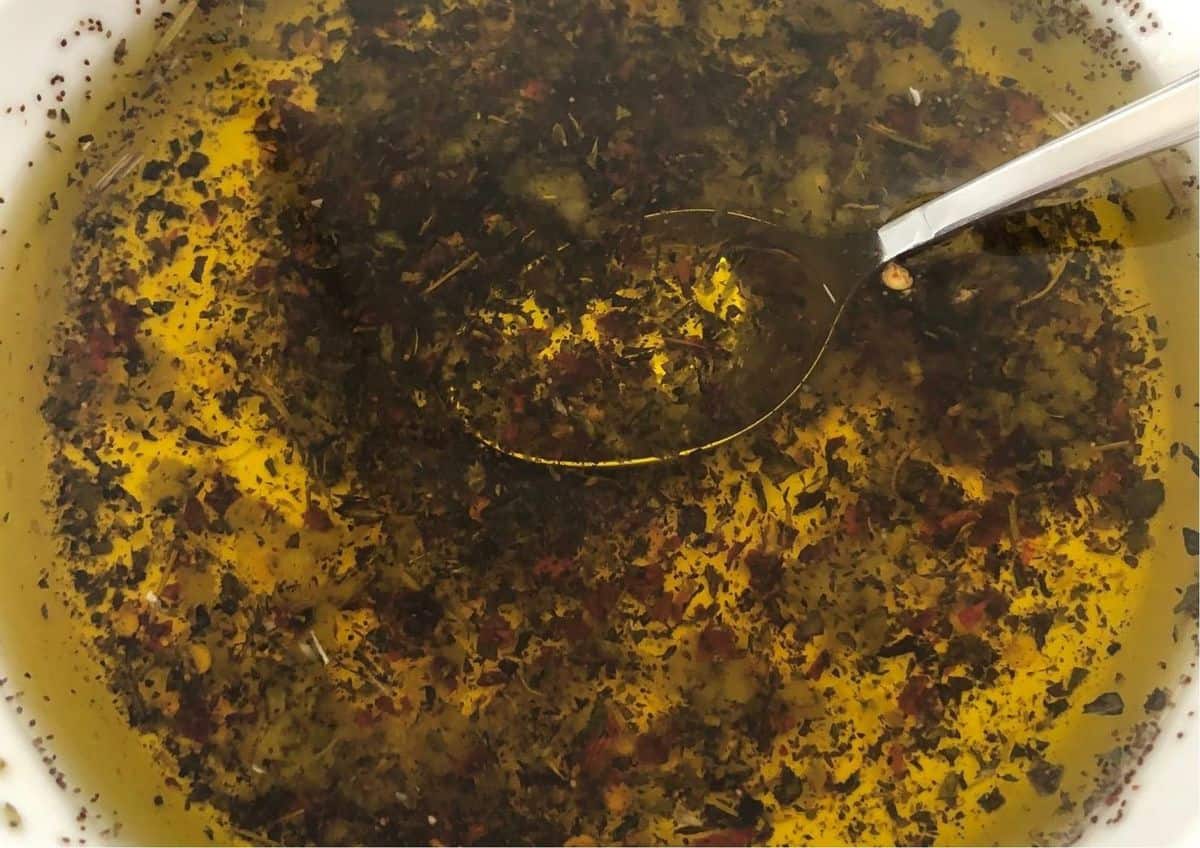 Up close shot of the dipping oil, with a silver spoon sitting in a white bowl.