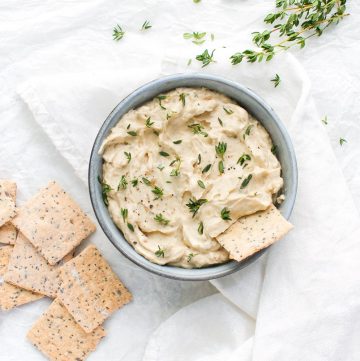 onion dip, on a white cloth background, with some crackers to the left of the bowl, and some sprigs of thyme to the right.