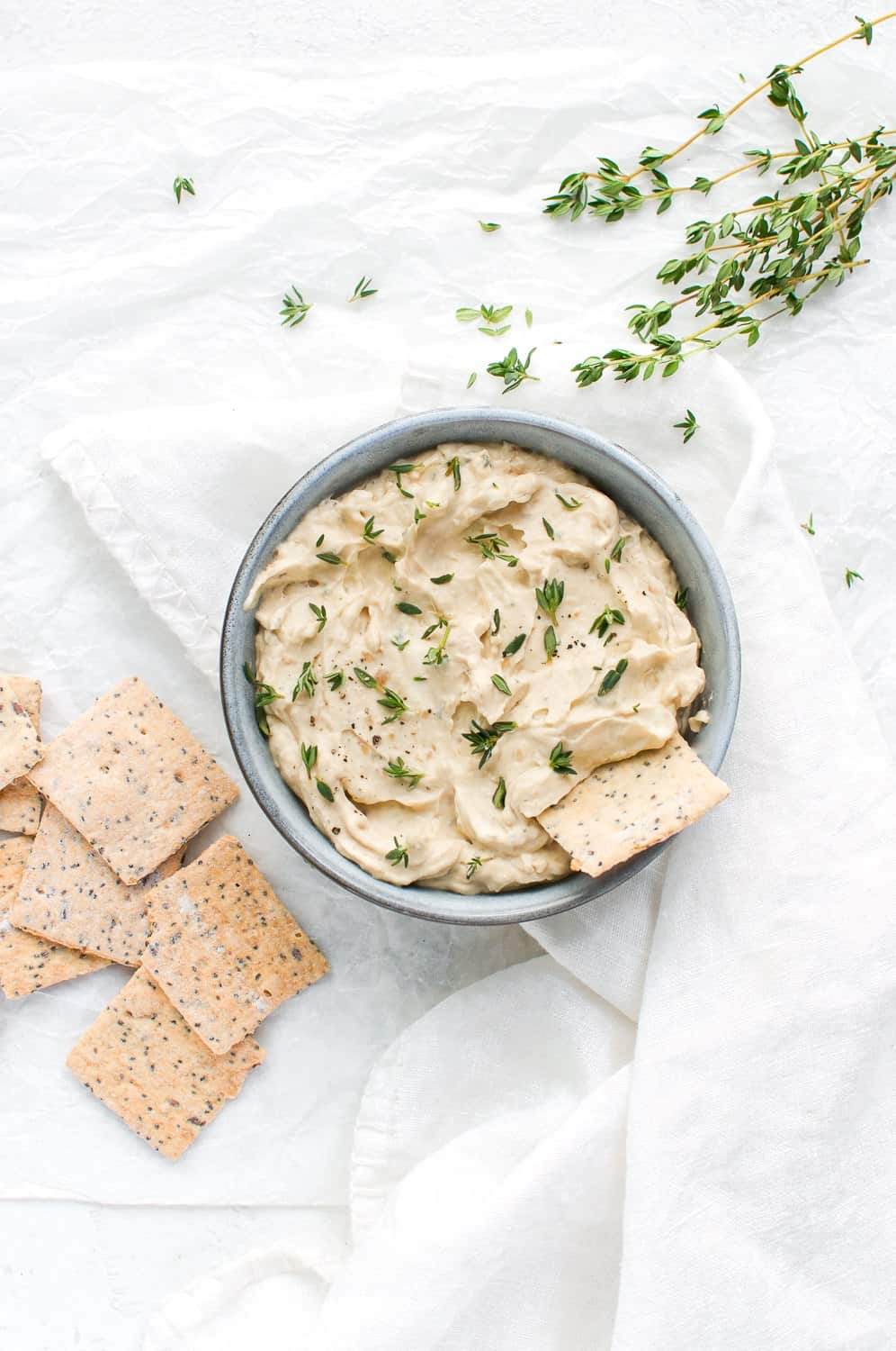 onion dip, on a white cloth background, with some crackers to the left of the bowl, and some sprigs of thyme to the right.