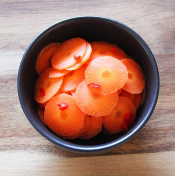 round black bowl of pickled carrots sitting on a wooden board.