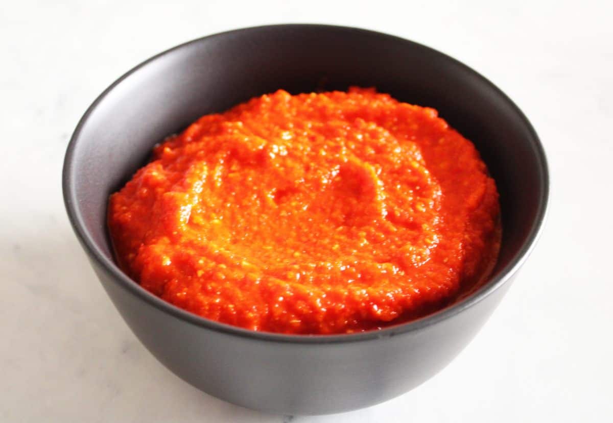 Black bowl, containing red chilli paste, on a white background.