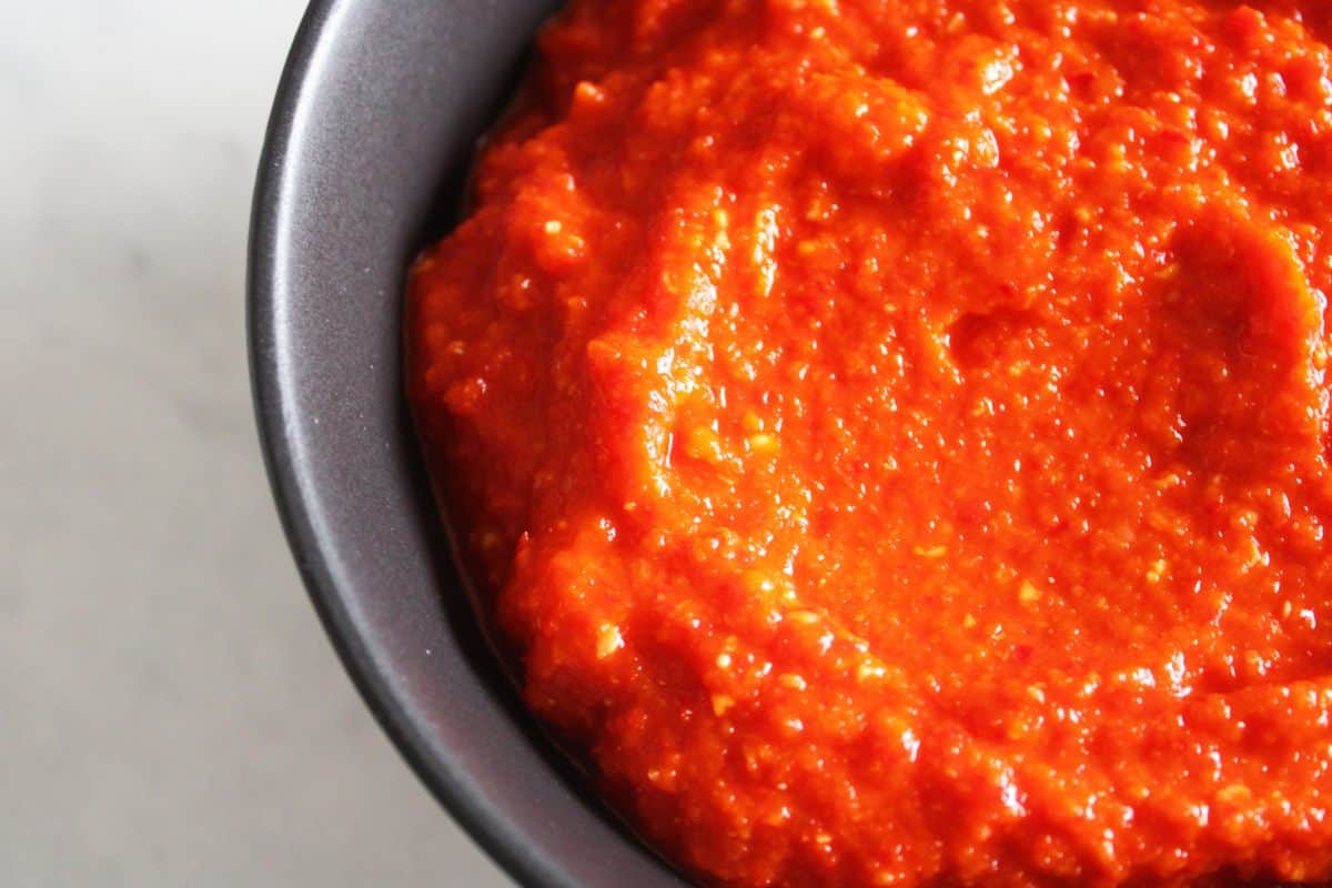 Up close shot of a half bowl of red chilli paste on a white background.