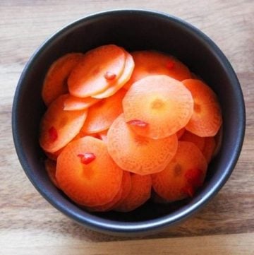 round black bowl of pickled carrots sitting on a wooden board.