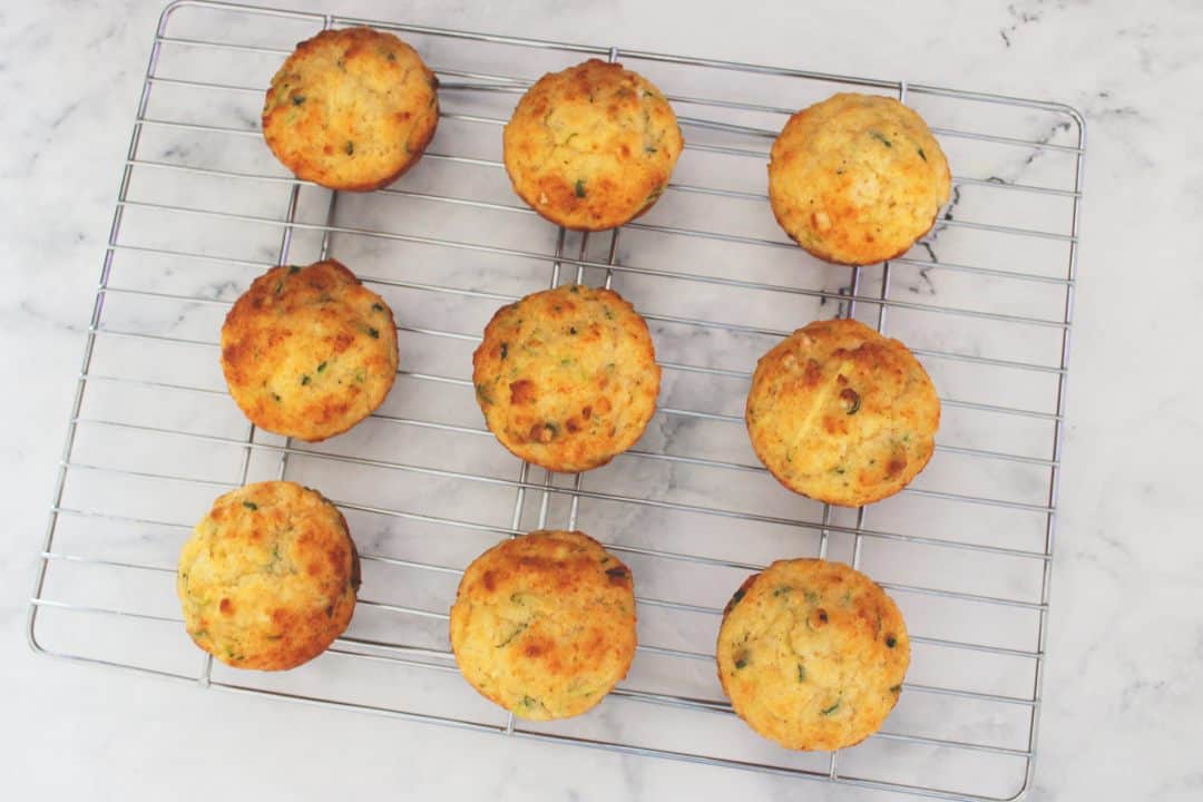 nine muffins sitting on a cooling rack, on a white marble background.