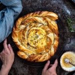 puff pastry spiral, with a hand on left hand side, and blue cloth in background.