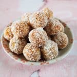 small round white and pink plate with bliss balls, sitting on a pink and white marble background.