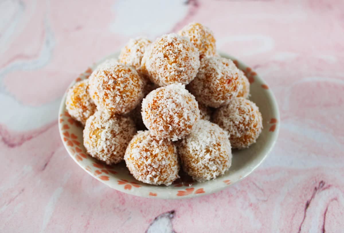 small round white and pink plate with bliss balls, sitting on a pink and white marble background.