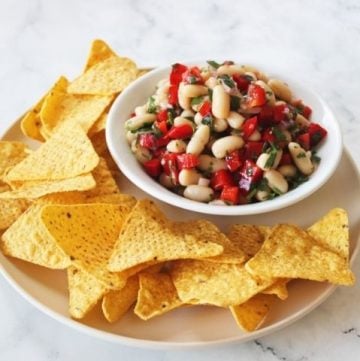 round beige plate with bowl of salsa and corn chips on a white marble background.