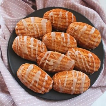 small round black plate of madeleines on a pink and white stripe tea towel, sitting on a marble bench.