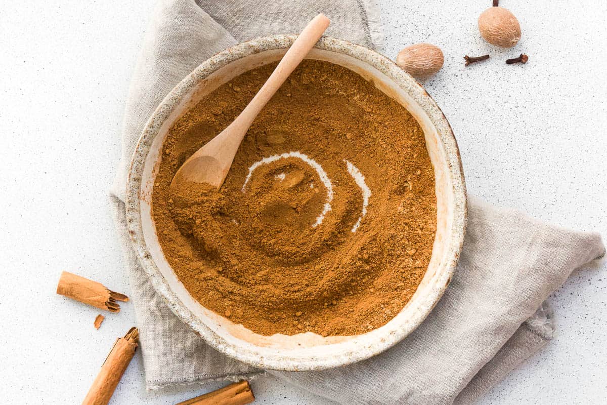 small flat stone bowl of mixed pumpkin spice, with a small wooden spoon on a grey cloth napkin.