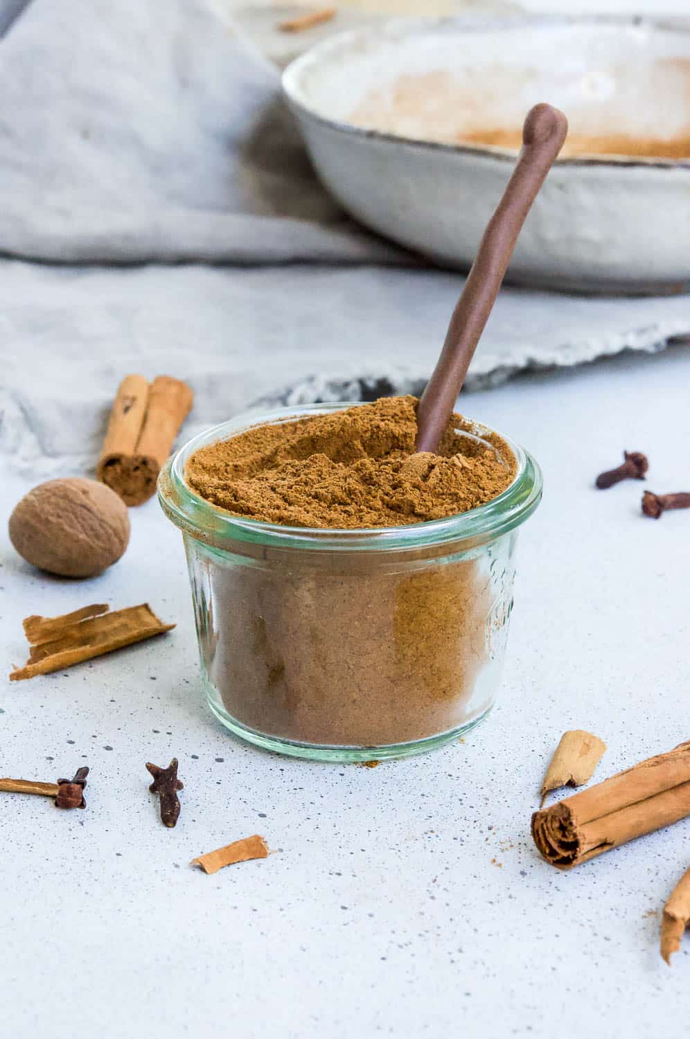 glass jar of pumpkin spice, with a wooden spoon scooping some, and some spices dotted around the edge of the photo frame.