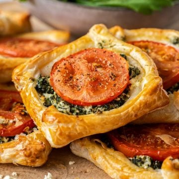 spinach galettes in a pile, on a wooden board, with a bowl of salad in the background.