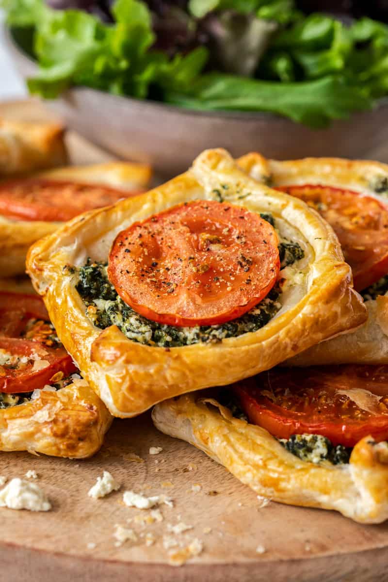 spinach galettes in a pile, on a wooden board, with a bowl of salad in the background.