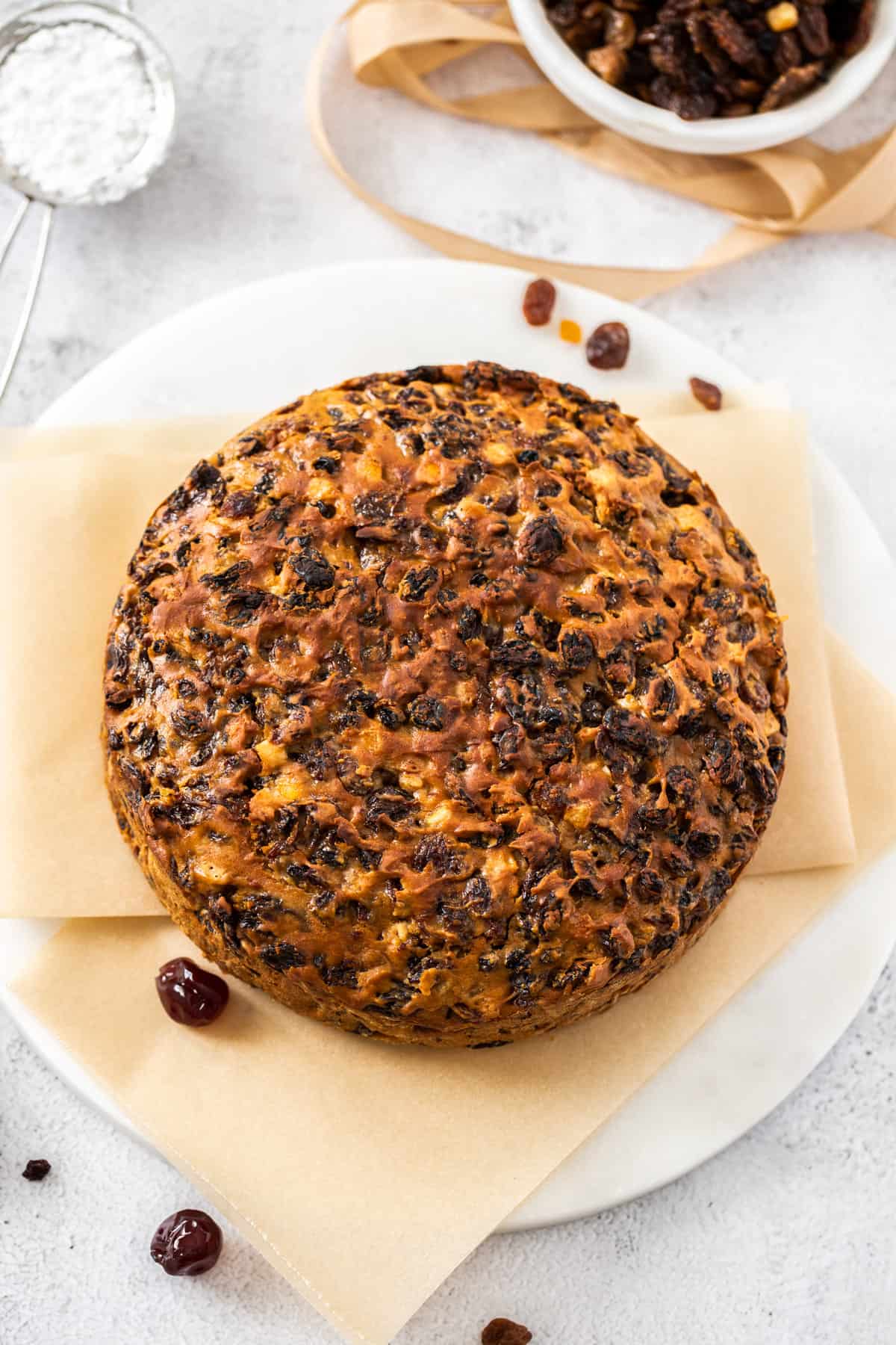 whole fruit cake sitting on some baking paper on a round white plate.