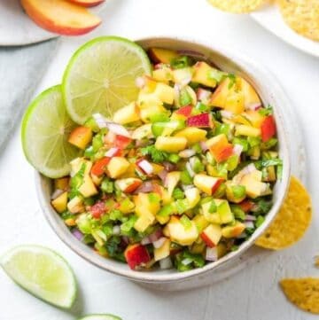 Bowl of salsa, garnished with lime slices, surrounded by some lime wedges and corn chips.
