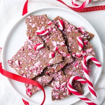 Chocolate Bark on a round white plate, decorated with some candy canes and some red ribbon.