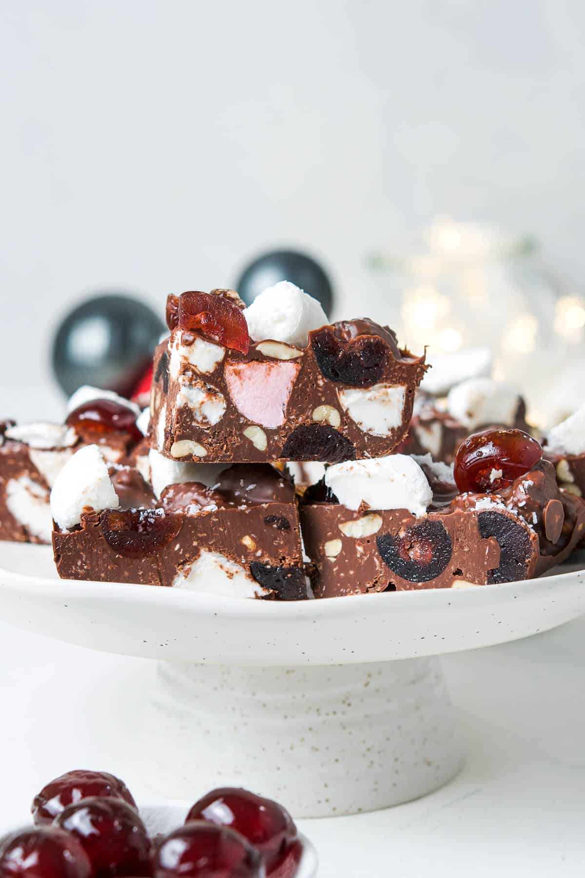 round white plate topped with rocky road with a bowl of cherries at the front.