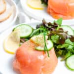 salmon parcel, on white plate, with salad on the side and a lemon garnish, another plate with same sitting in background.
