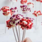 a hand holding up some coated and decorated marshmallows with more in the background.