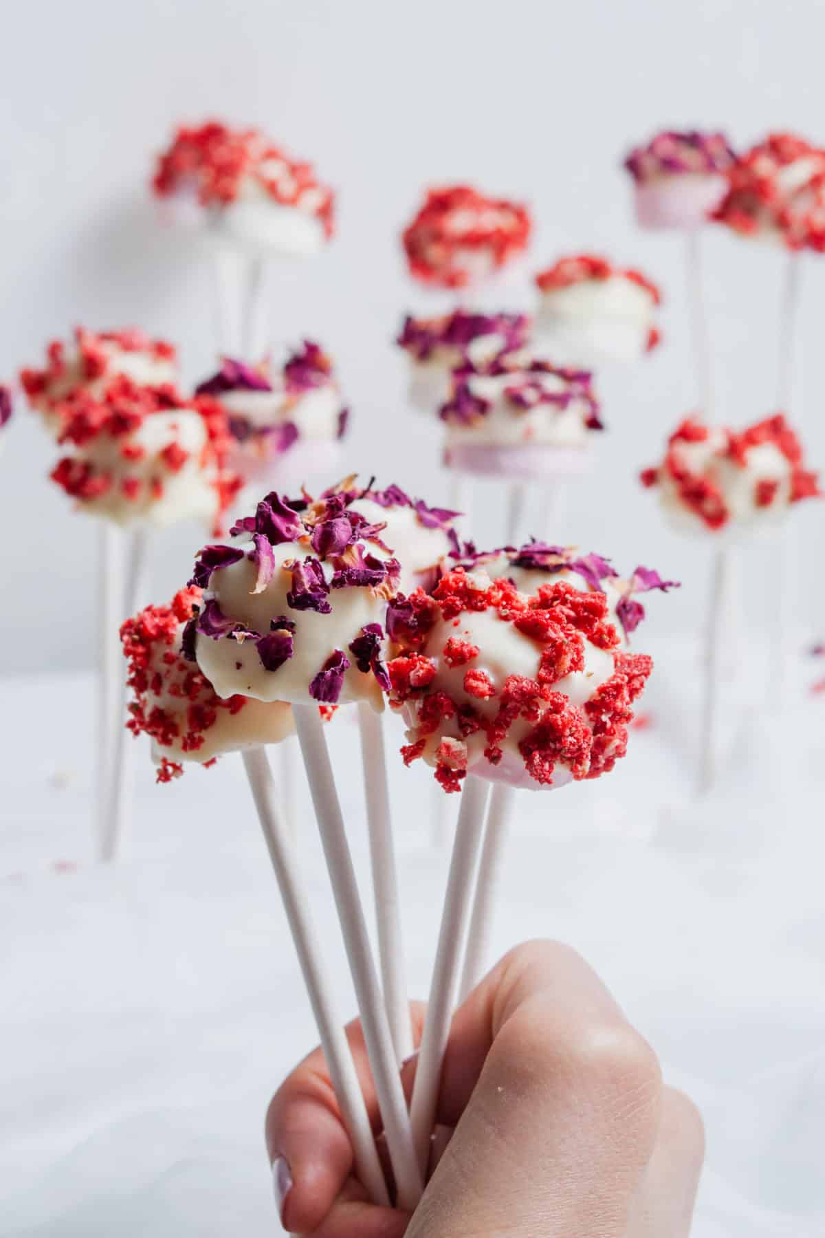 a hand holding up some coated and decorated marshmallows with more in the background.