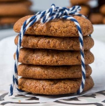 Stack of cookies, tied with a blue and white string, sitting on a white tile, with cookies in the background.