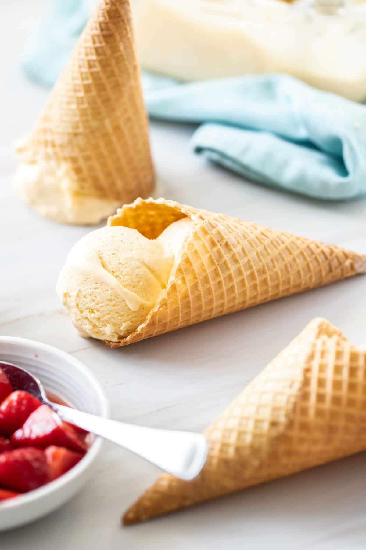 three ice cream cones, one with ice cream, with a bowl of strawberries on the side.