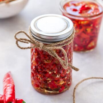 jar of chillies with lid, tied with some string, and some jars and a bowl of chillies in the background.