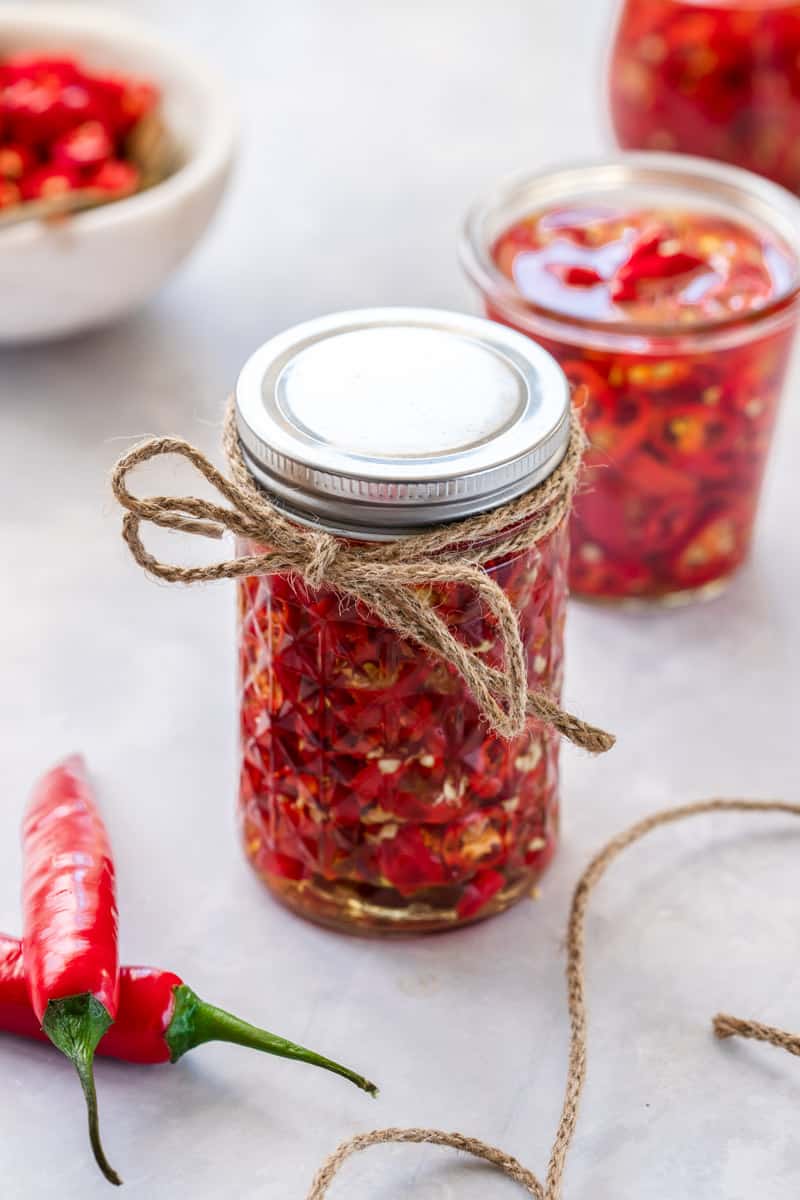jar of chillies with lid, tied with some string, and some jars and a bowl of chillies in the background.