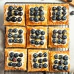 tarts sitting on a cooling rack, topped with blueberries and lemon zest.