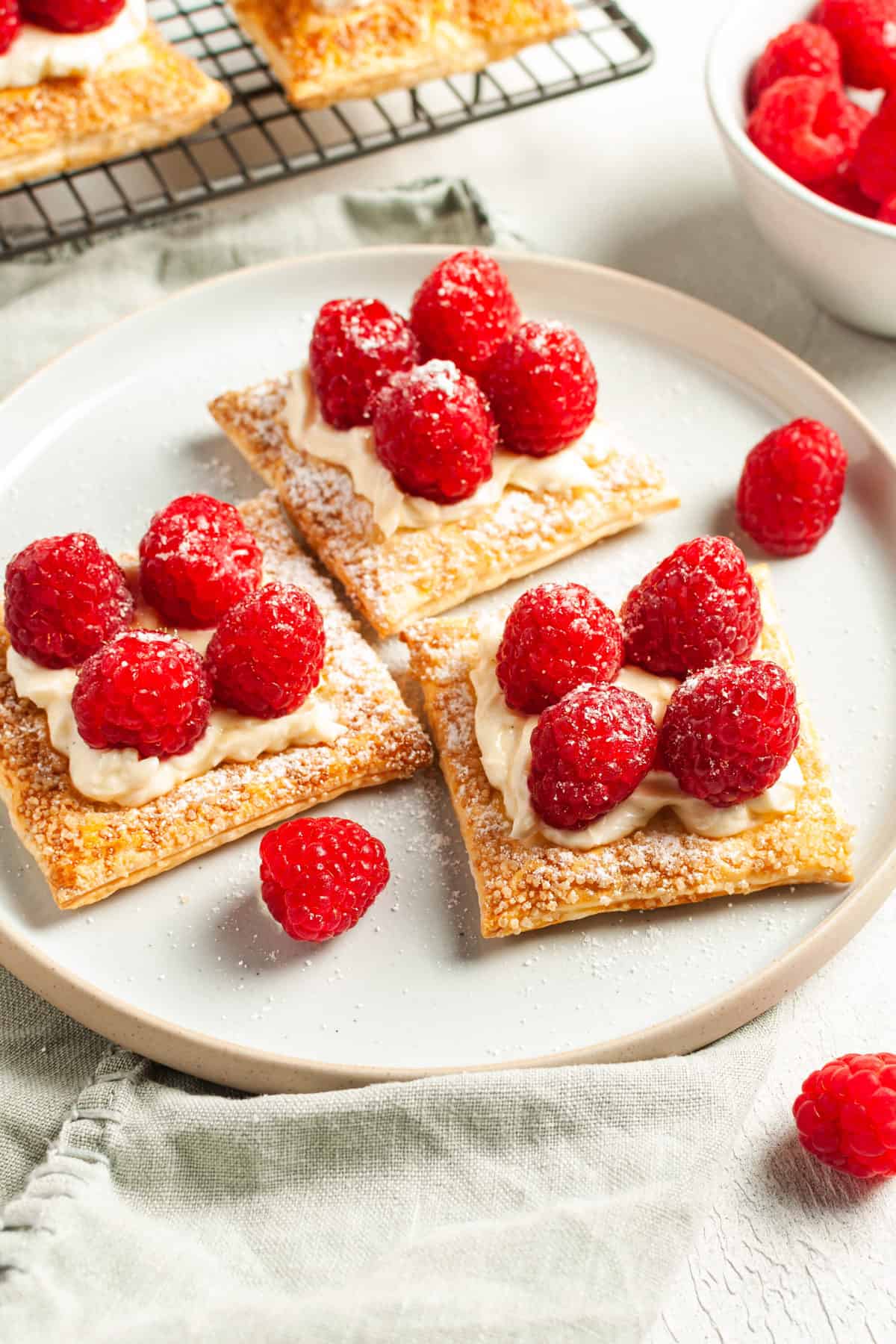 three tartlets sitting on a round white plate, with some raspberries around the edge.