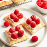 three tartlets on a round white plate, with a couple of raspberries around the edge.