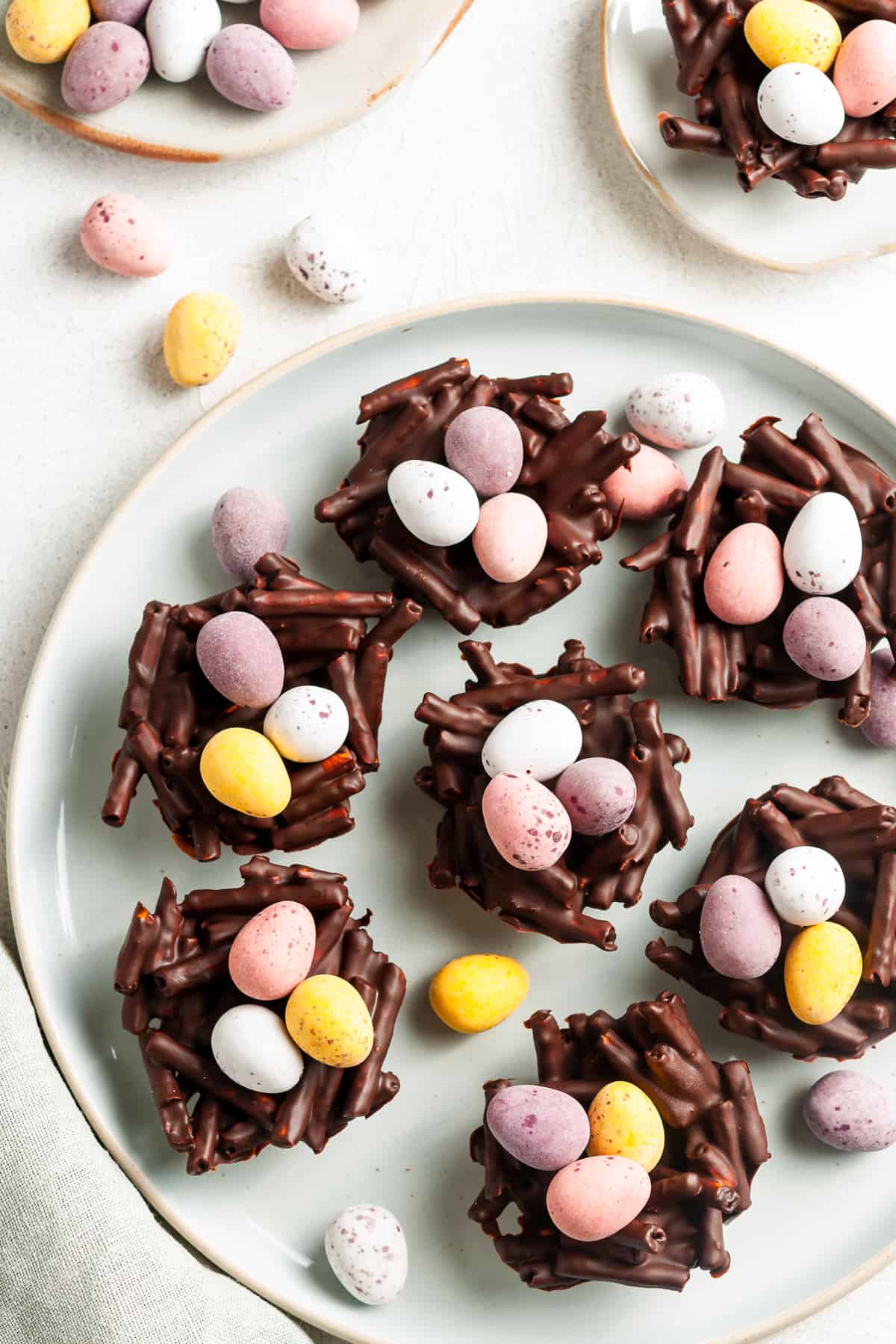 overhead shot of round white plate with easter nests filled with mini eggs, with some more mini eggs around the edge.