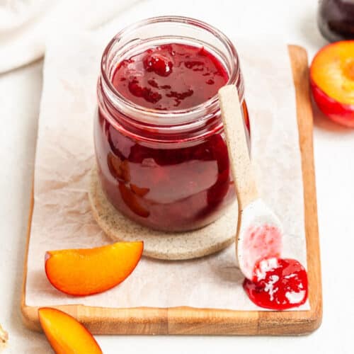 Jar of jam, sitting on a board, with a spoon and a dollop of jam on the edge.
