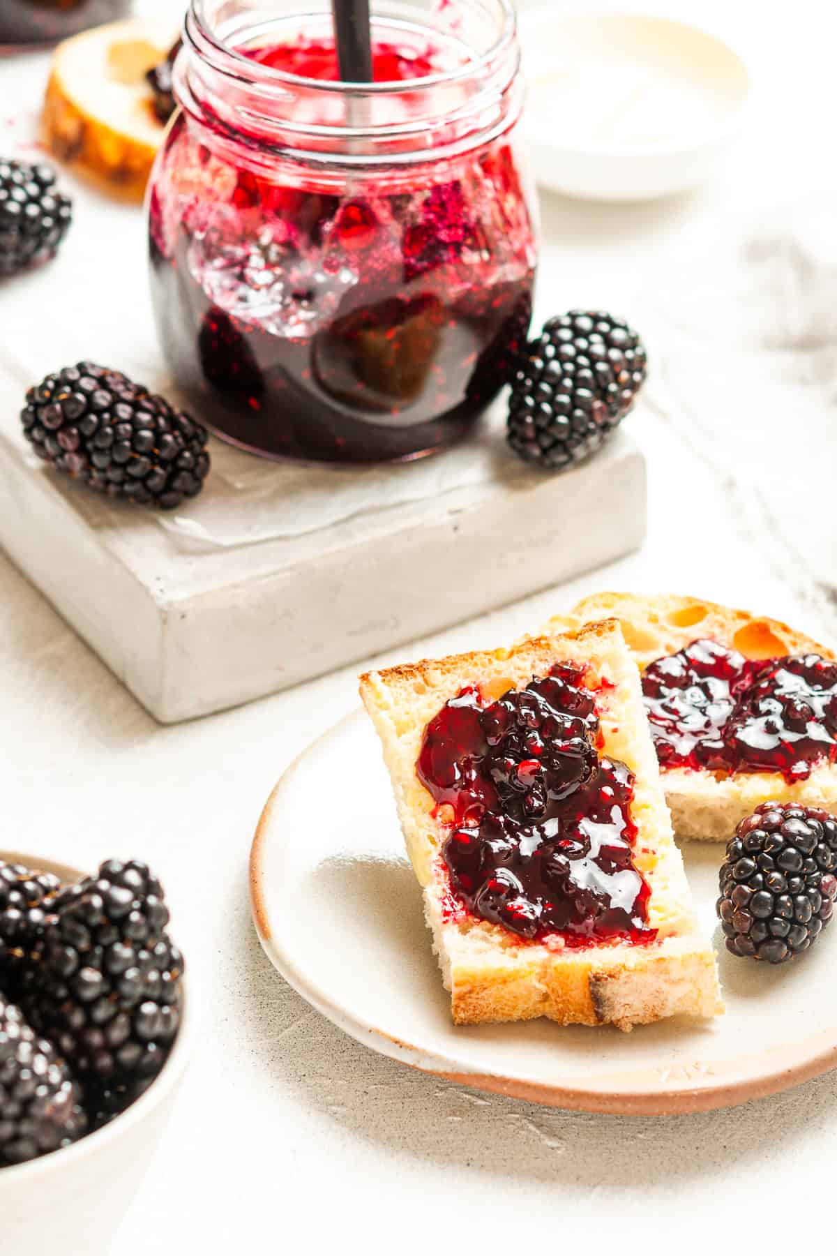 Plate with some toast topped with jam, and a jar of jam and some blackberries in the background.