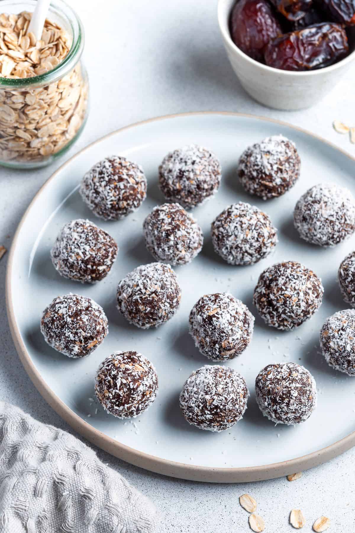 Round plate of bliss balls, with a jar of oats, a dish of dates and a cloth around the edge.