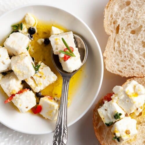 Up close shot of dish of feta, with spoon in it, and some slices of bread around the edge.