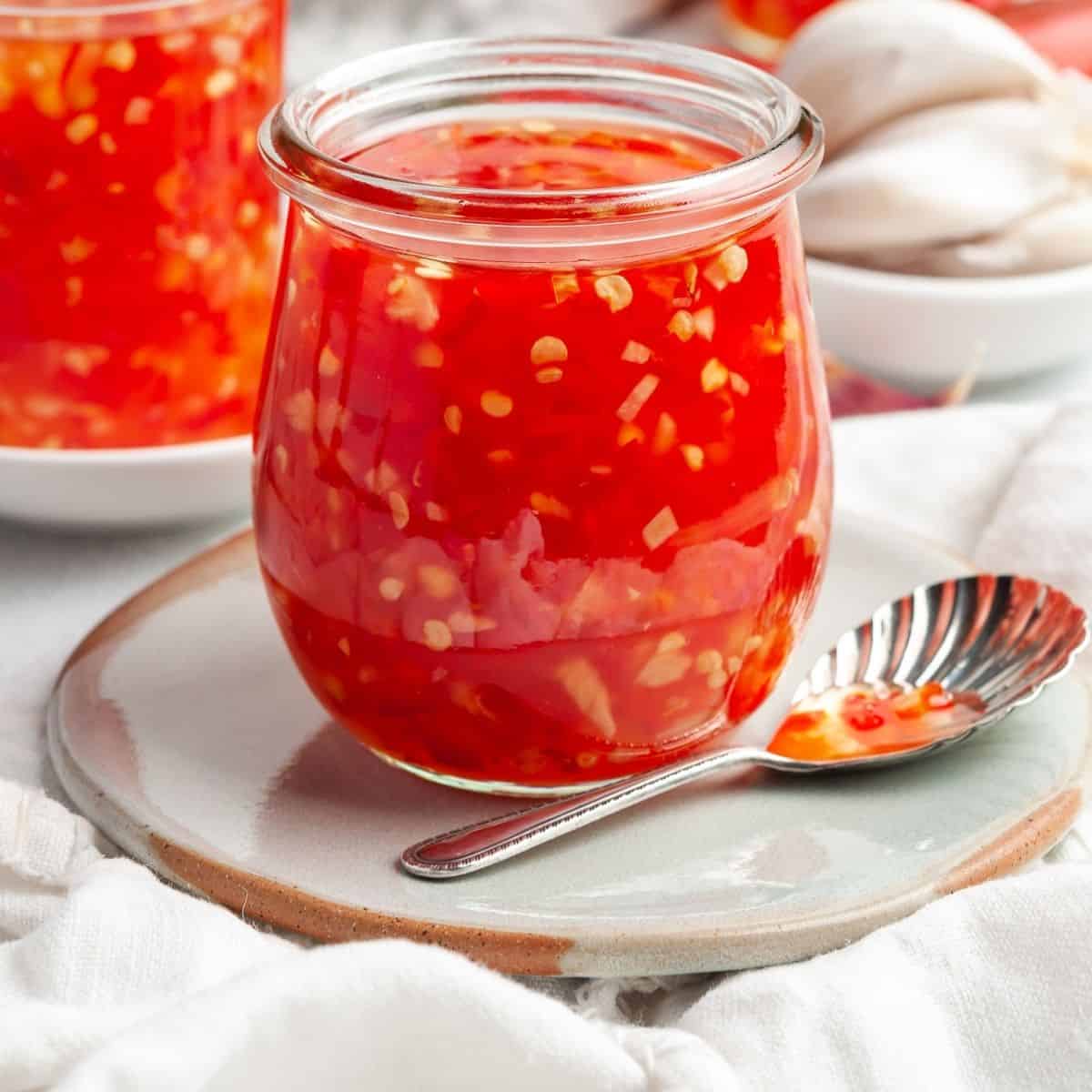 Up close shot of small pot of sauce, sitting on a saucer with a spoon on the side.